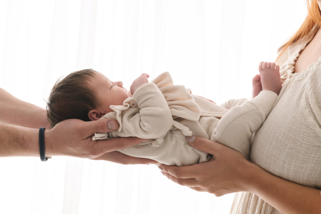 studiofoto van newborn baby meisje gedragen in de handen van mama en papa gefotografeerd door Digidroom in Malle