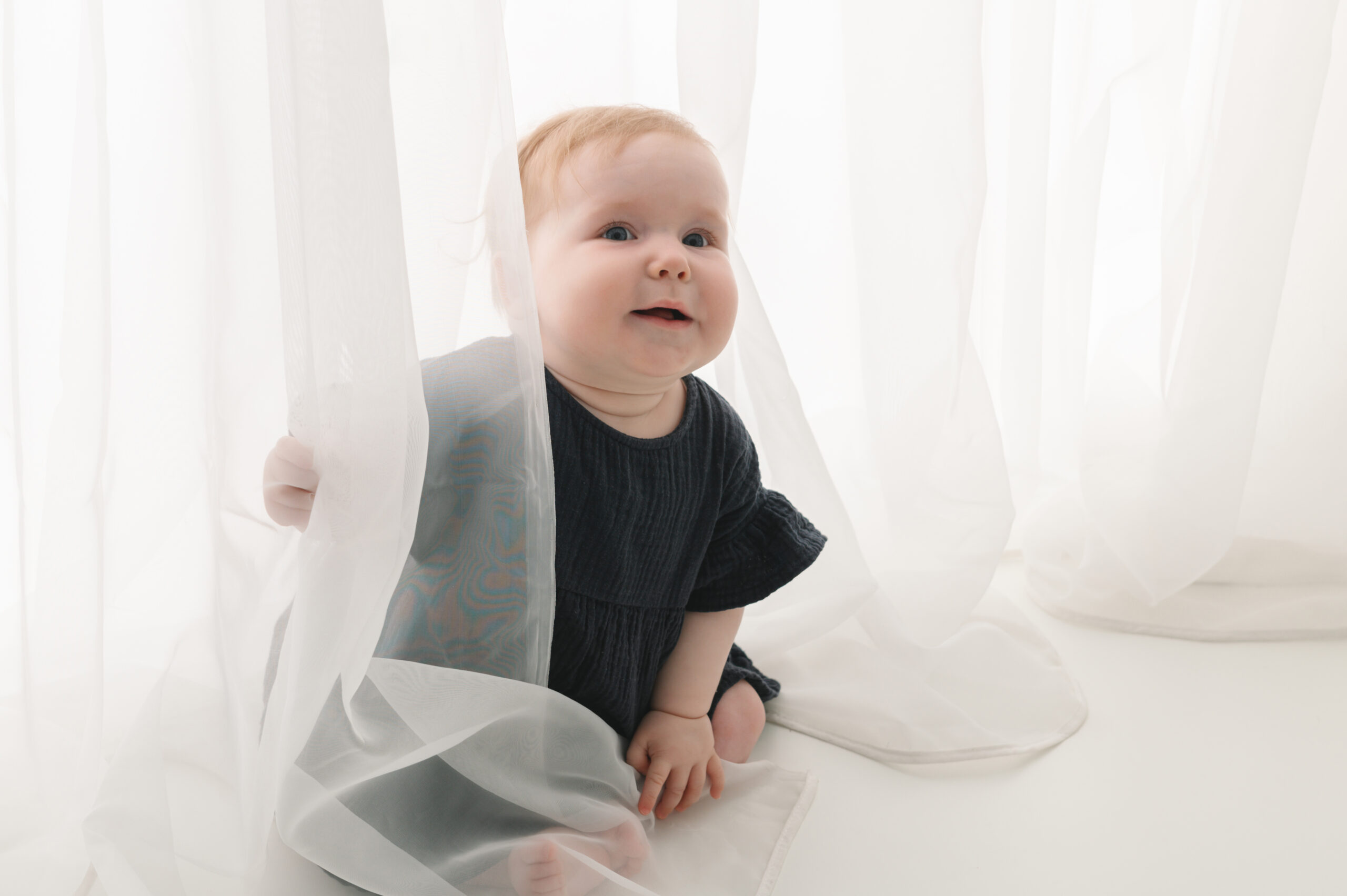 baby die zit en verstoppertje speelt aan gordijn