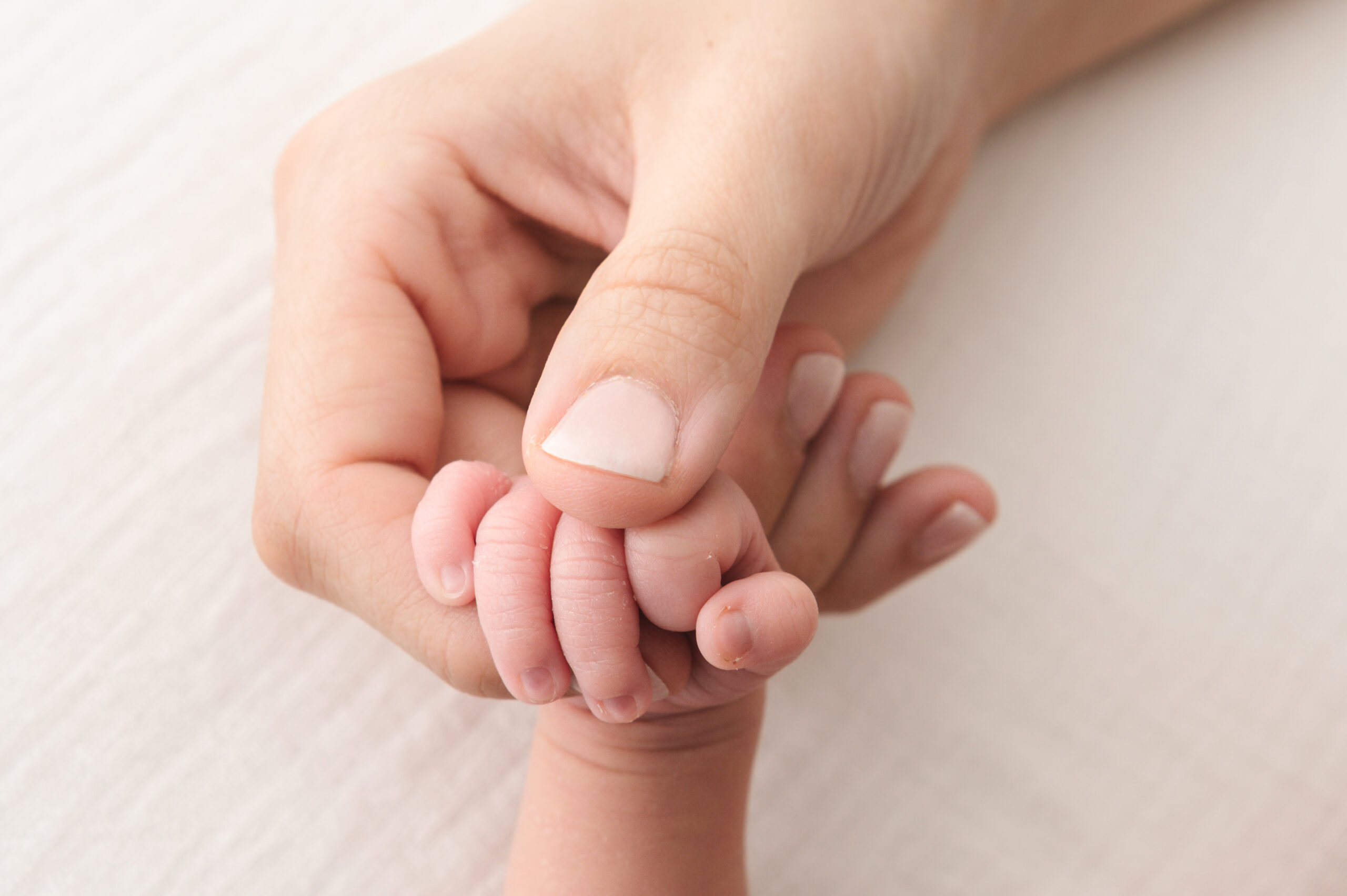 Close-up van een mama die het handje van haar 3 maanden oude baby vasthoudt – een tedere detailfoto die de liefdevolle band en de kleine details van een baby fotoshoot vastlegt.