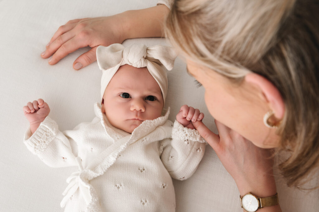 newborn babymeisje die mama's pink vasthoudt en haar liefdevol aankijkt in een rustige neutrale setting, gefotografeerd door Digidroom